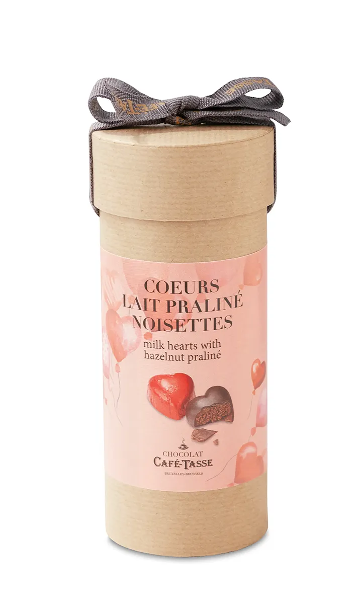 Tube cadeau en carton kraft Café-Tassé fermé par un ruban gris noué, étiquette rose « Coeurs Lait Praliné Noisettes » illustrée de bonbons cœur en chocolat.