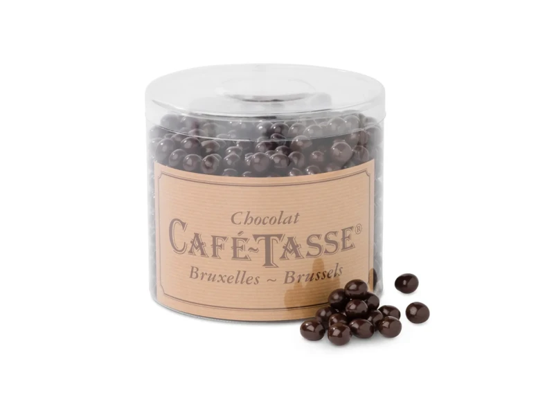 Pot distributeur transparent étiqueté « Chocolat Café-Tassé Bruxelles-Brussels » rempli de petites perles de chocolat rondes et foncées, quelques-unes versées devant le pot.