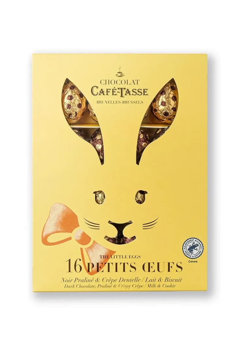 Boîte jaune Café-Tassé « Les Petits Oeufs » découpée en forme d'oreilles de lapin, laissant apparaître des œufs en chocolat emballés dans un papier alu doré et bordeaux à pois.