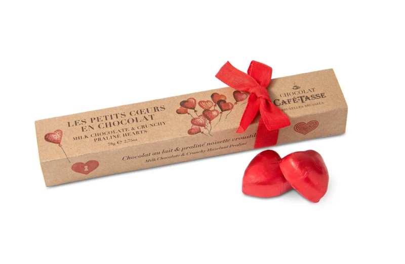 Boîte réglette kraft nouée d'un ruban rouge, illustration de cœurs en ballons, « Les Petits Cœurs en Chocolat » Café-Tassé au praliné noisette croustillant, 78 g, cœurs emballés rouges devant.