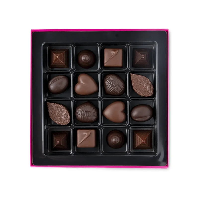 Boîte de pralines ouverte au coffret rose fuchsia, alvéoles noires garnies de chocolats de formes variées : pyramides, dômes, cœurs, feuilles et coques, assortiment Perlège.