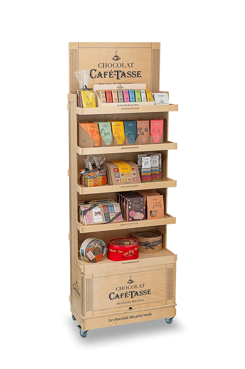 Présentoir en bois clair à plusieurs étagères, plaque « Chocolat Café-Tassé Bruxelles-Brussels », garni de rangées de mini tablettes multicolores et de sachets emballés.