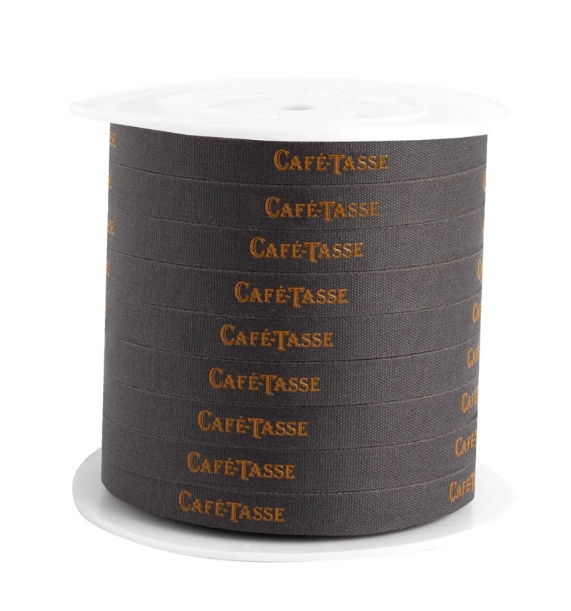 Bobine de ruban textile gris anthracite tissé du mot « Café-Tassé » en lettres dorées répété sur toute la longueur, présentée sur son mandrin blanc, ruban 10mm 200m.