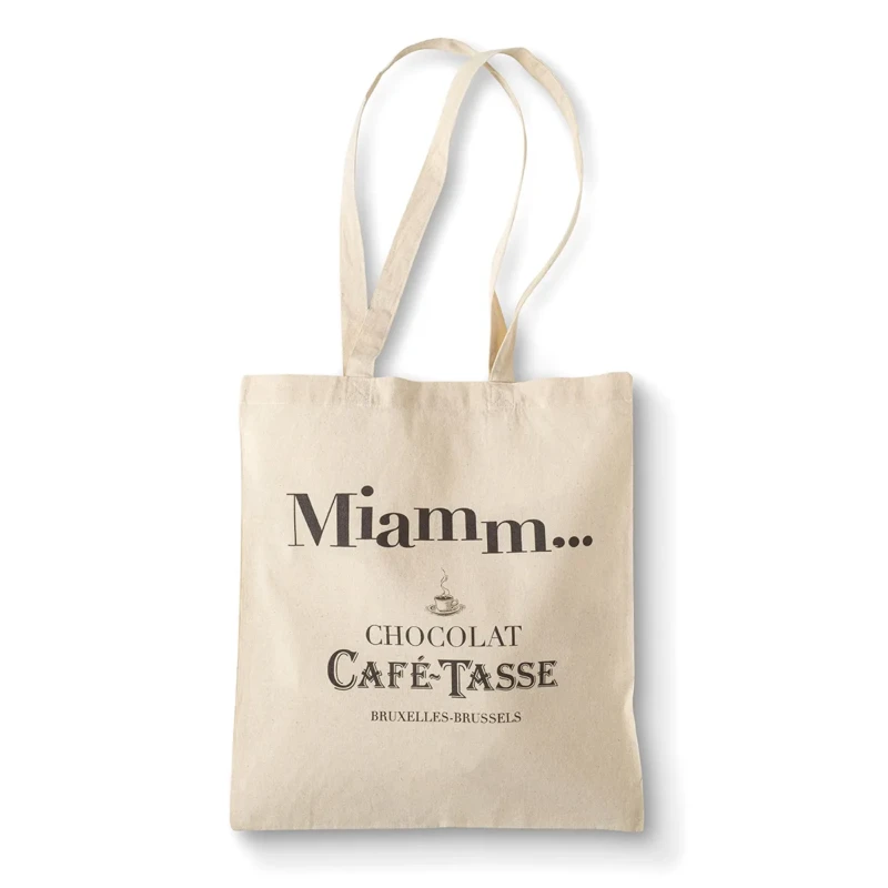 Tote bag en toile beige à longues anses, imprimé « Miamm... » et « Chocolat Café-Tassé Bruxelles-Brussels » en lettres brunes, posé à plat sur fond blanc.